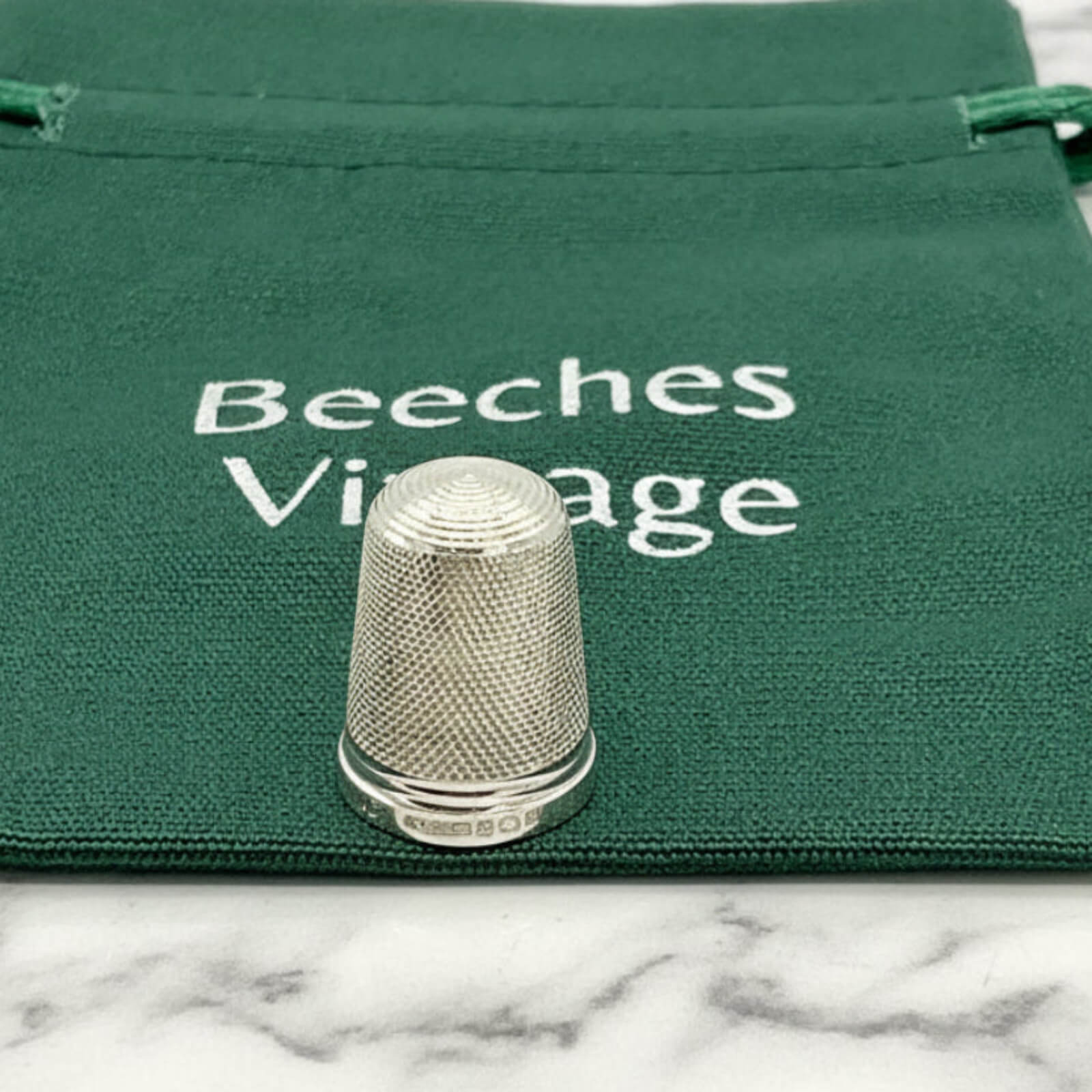 Silver thimble on a green fabric bag with 'Beeches Vintage' text.