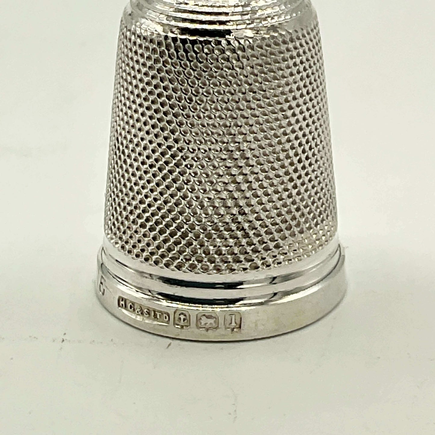 close up of hallmarks on silver thimble on white background