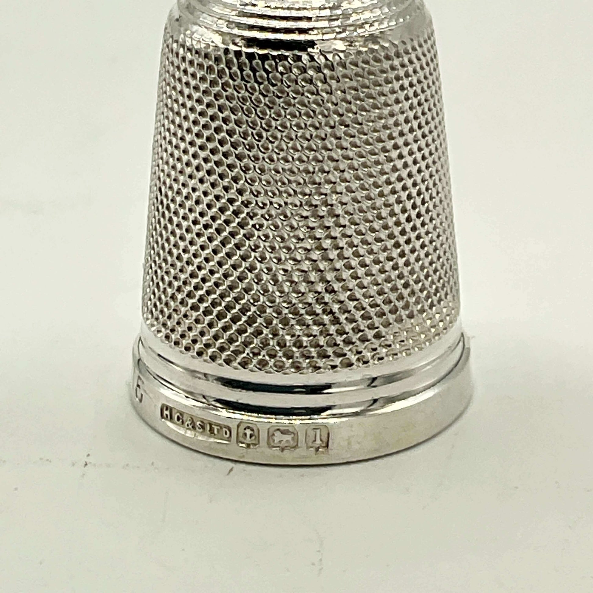 close up of hallmarks on silver thimble on white background