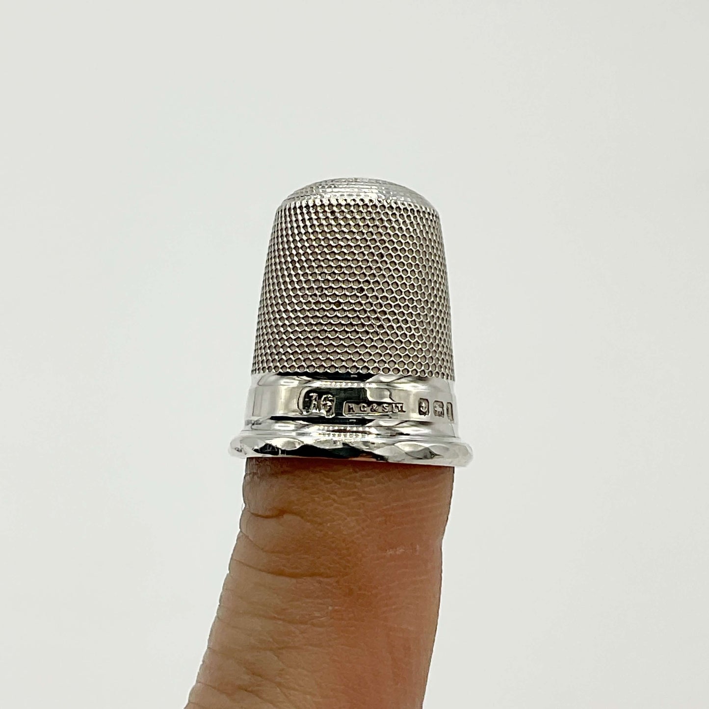 Silver thimble on a finger against a white background showing the hallmarks and 16 for the size