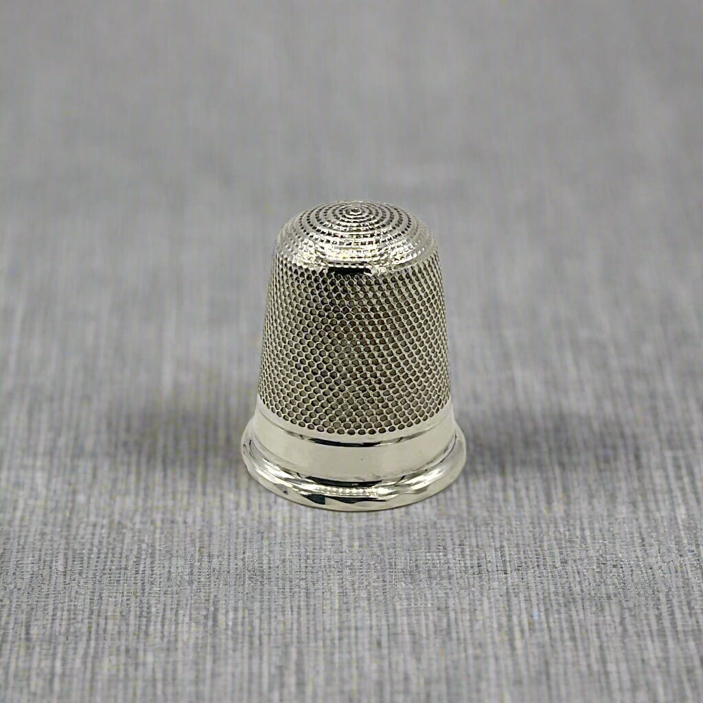 Silver thimble on a textured grey background