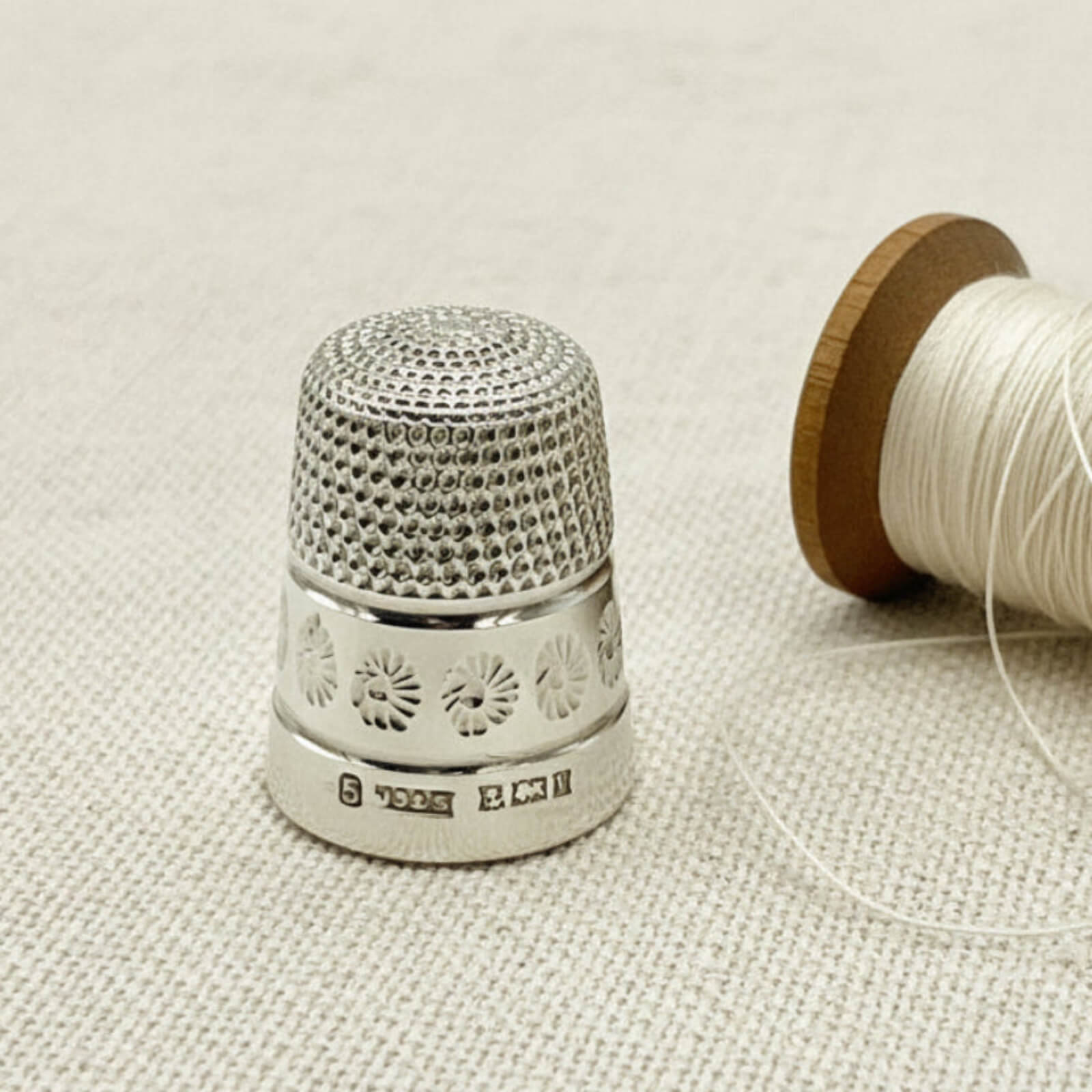 Silver thimble with floral patterns on a beige fabric background