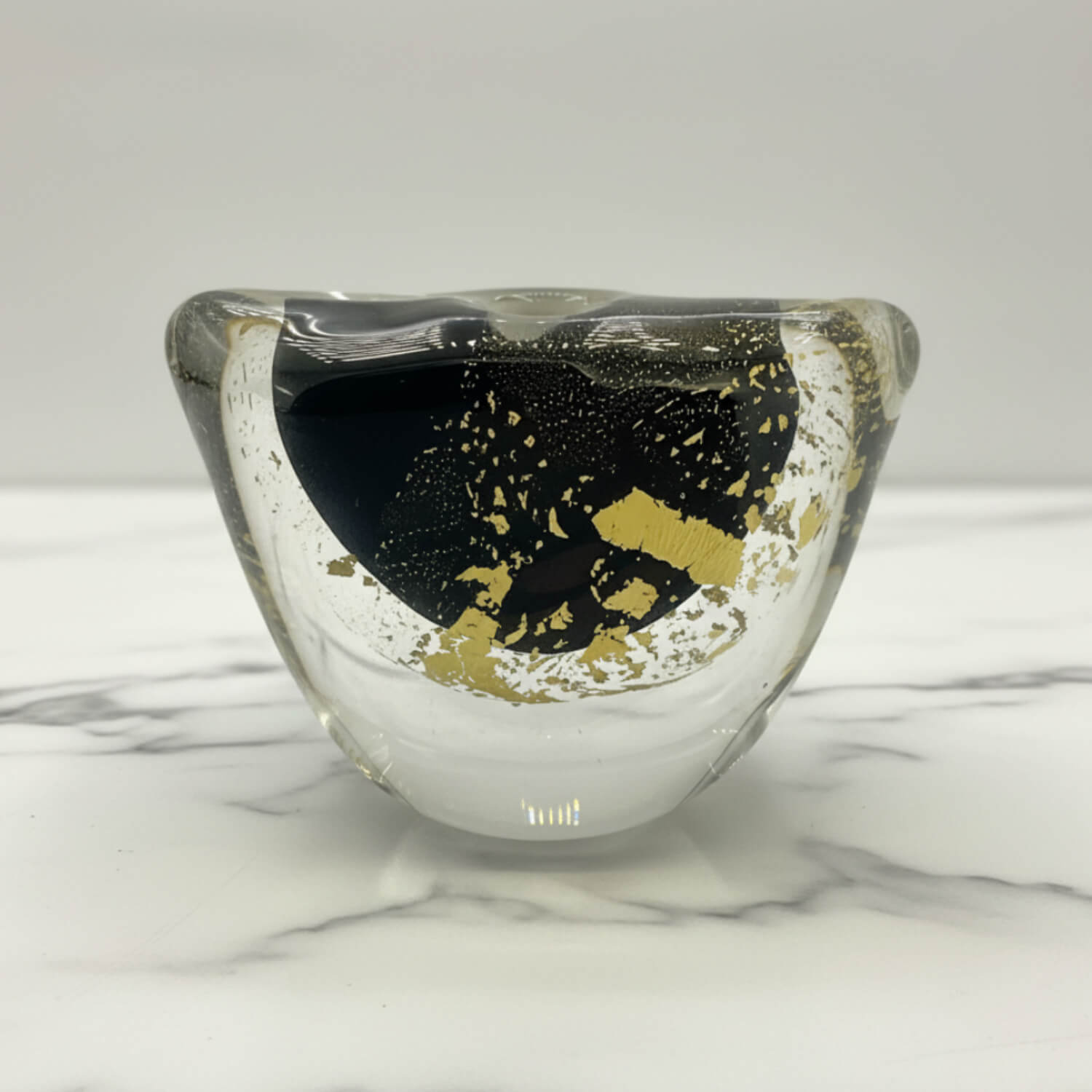 A clear glass vase with a black and gold abstract pattern inside, displayed on a white marble surface against a light gray background.