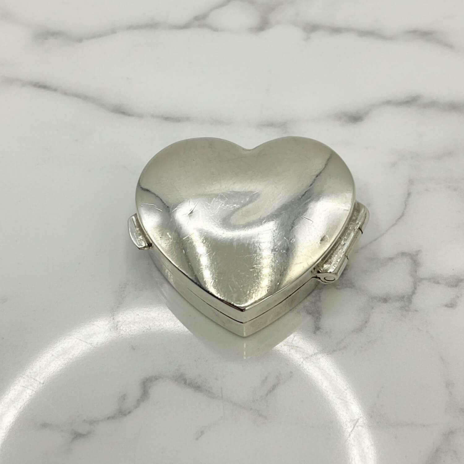 Heart-shaped silver pill box on a marble surface