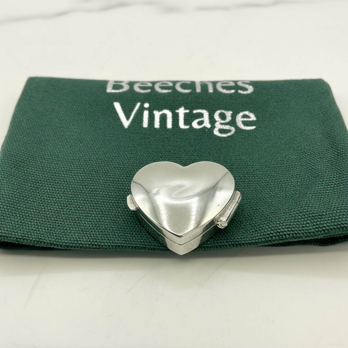 Silver heart-shaped pill box on a green Beeches Vintage pouch