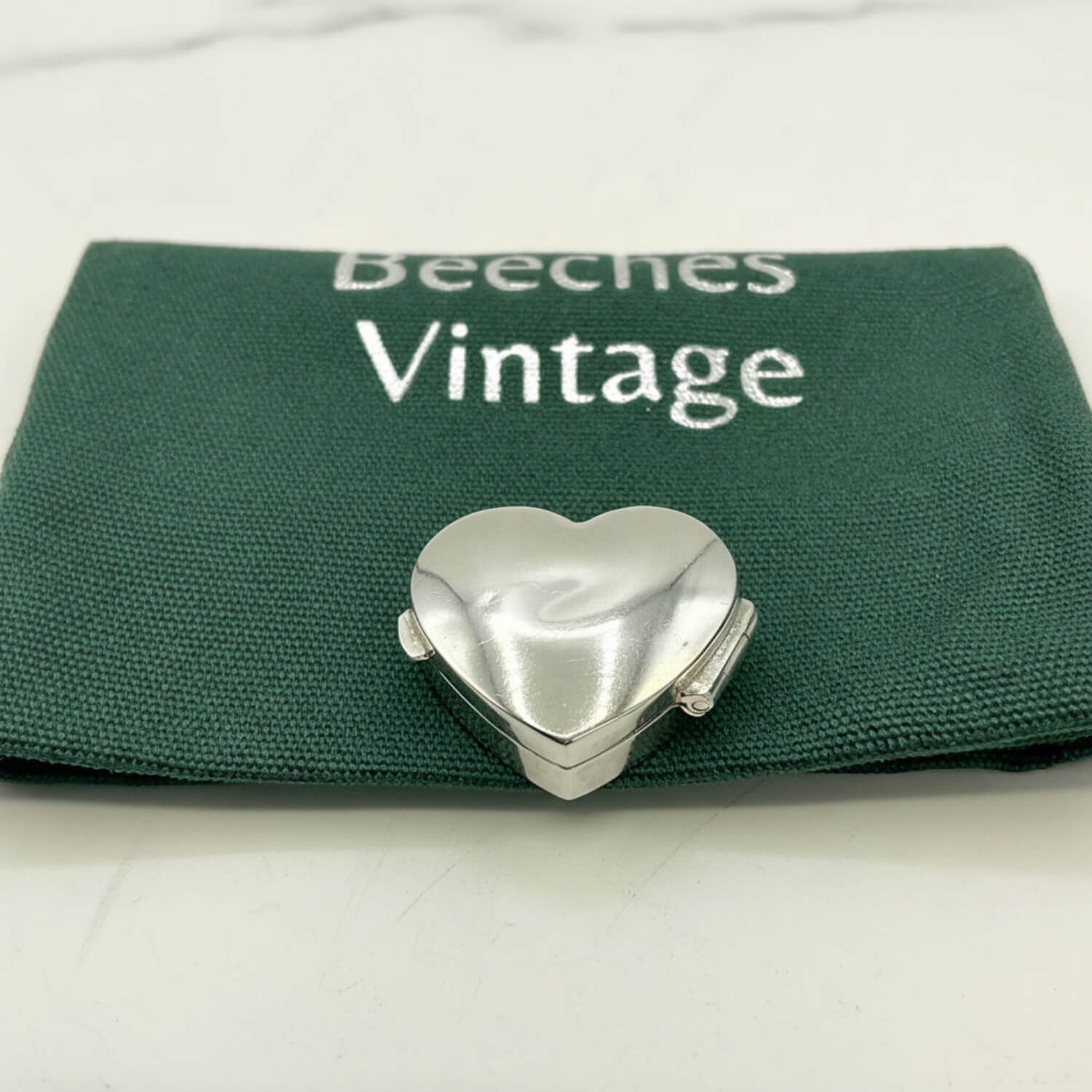 Silver heart-shaped pill box on a green Beeches Vintage pouch