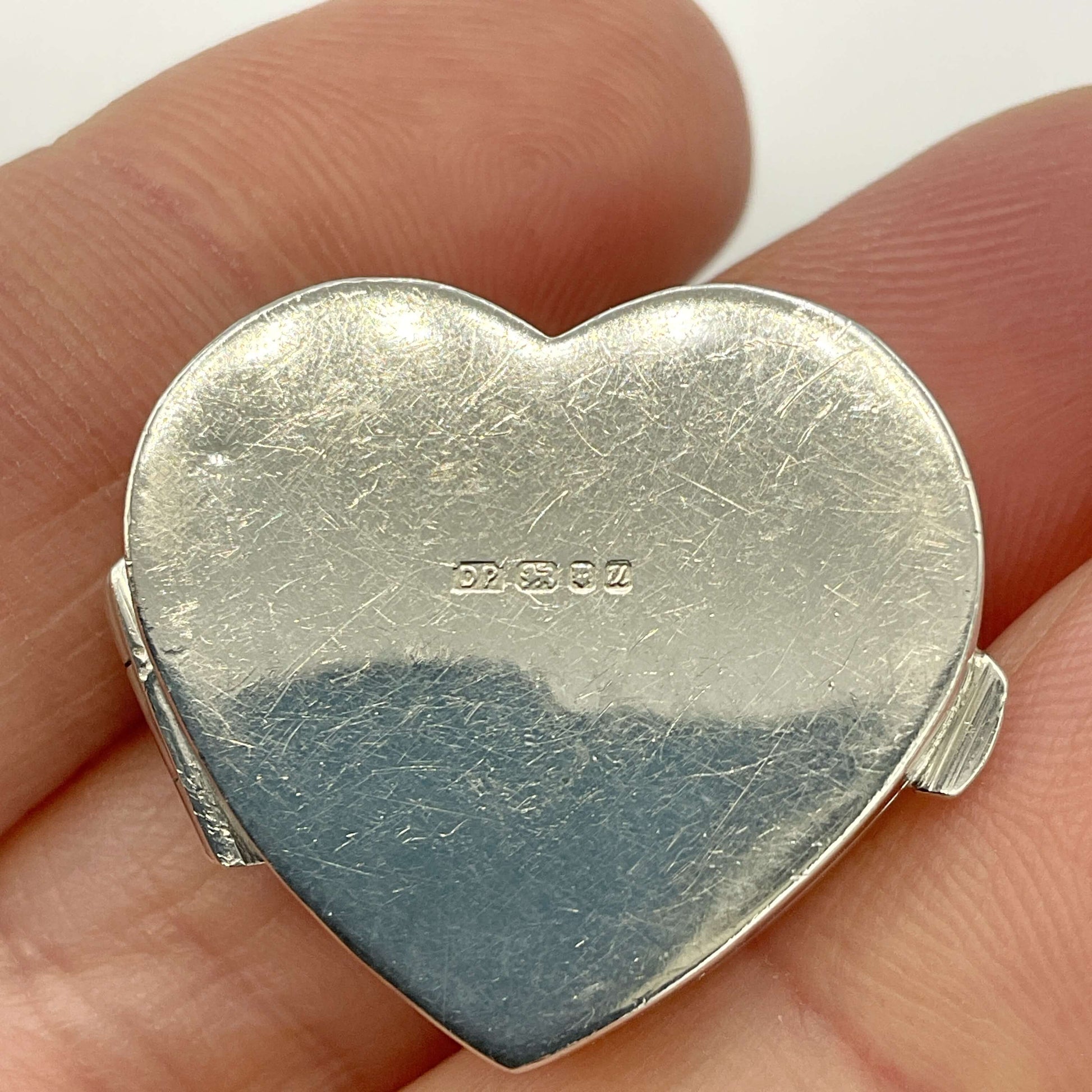 Silver heart-shaped pill box base with visible hallmarks held between fingers