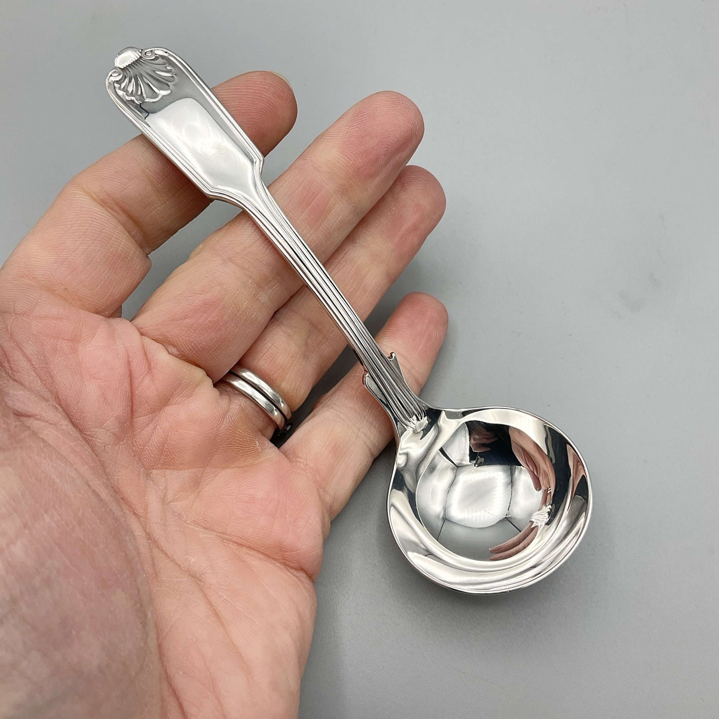 Small Silver Plated Sauce Ladle held in a hand with a grey background