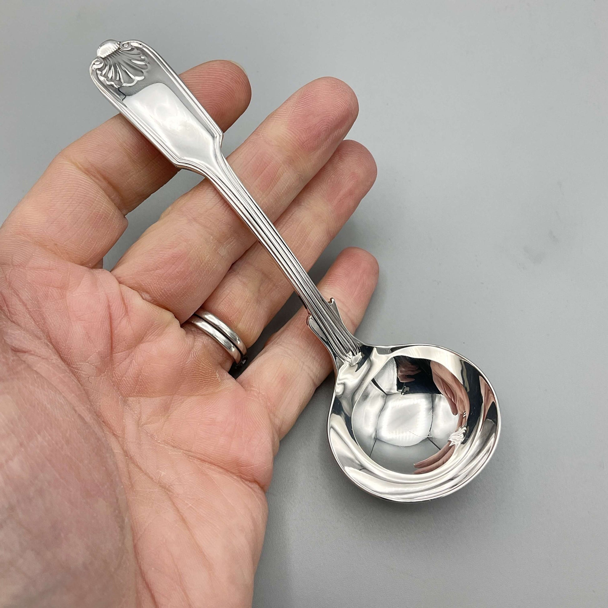 Small Silver Plated Sauce Ladle held in a hand with a grey background