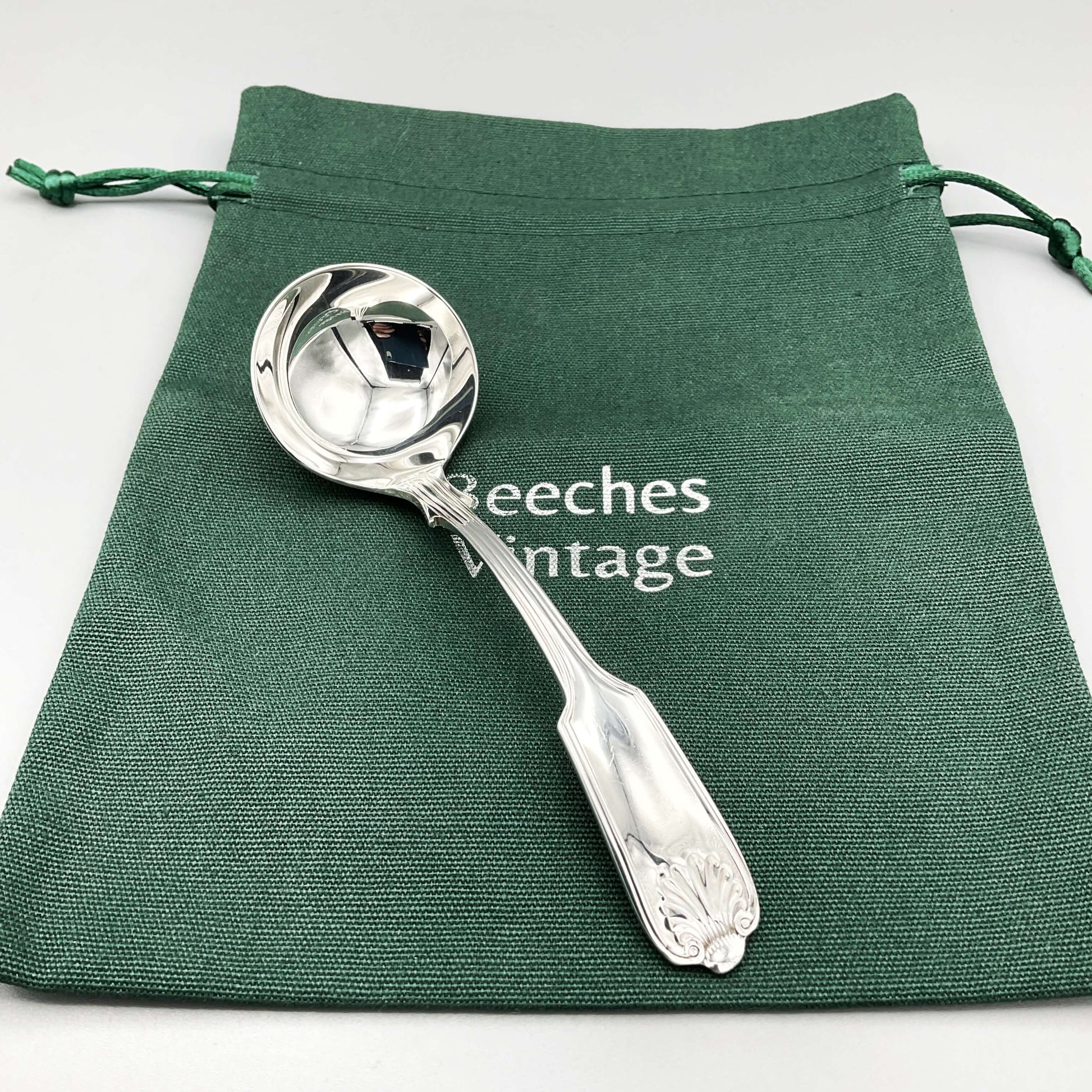 Small Silver Plated Sauce Ladle on a green gift bag with a grey background