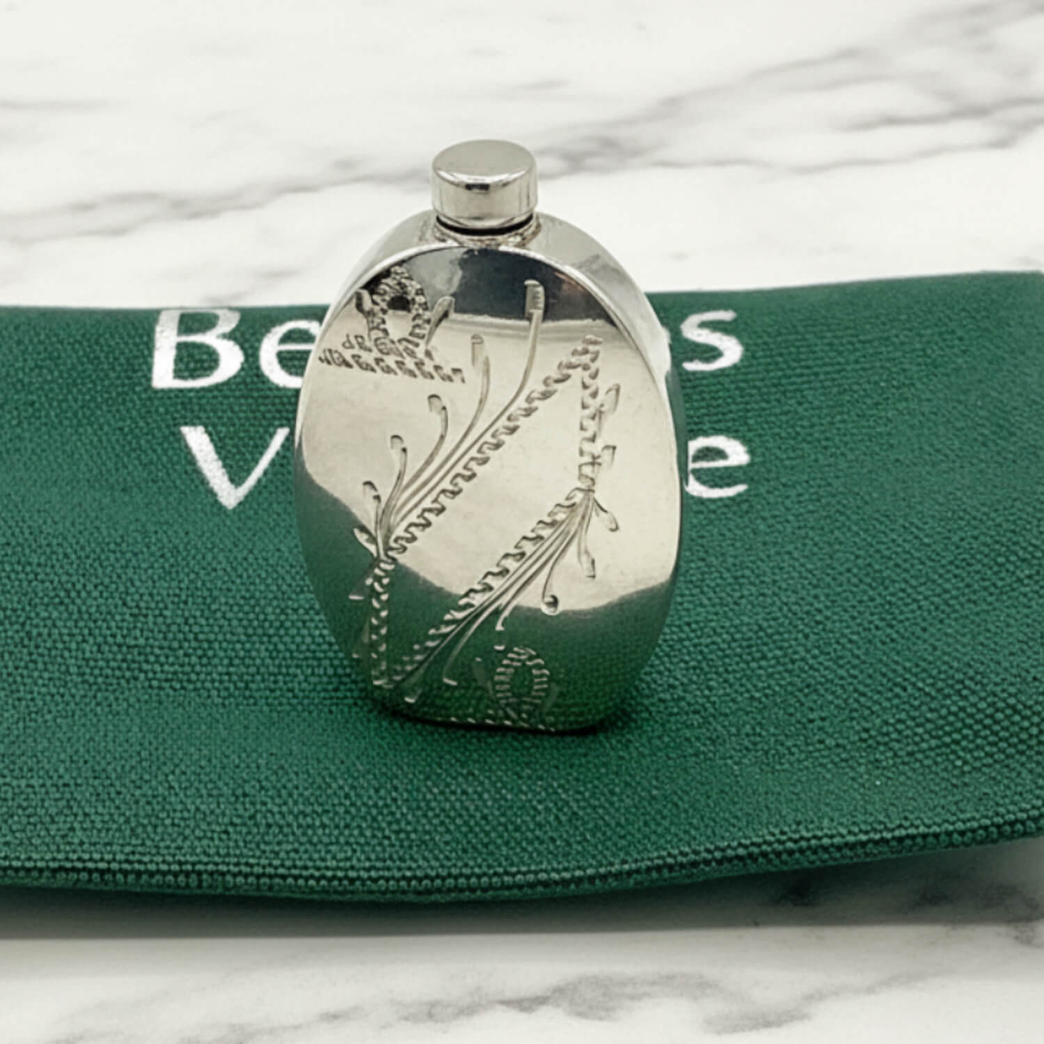 Small Sterling Silver Scent Bottle with engraved design on a green bag background