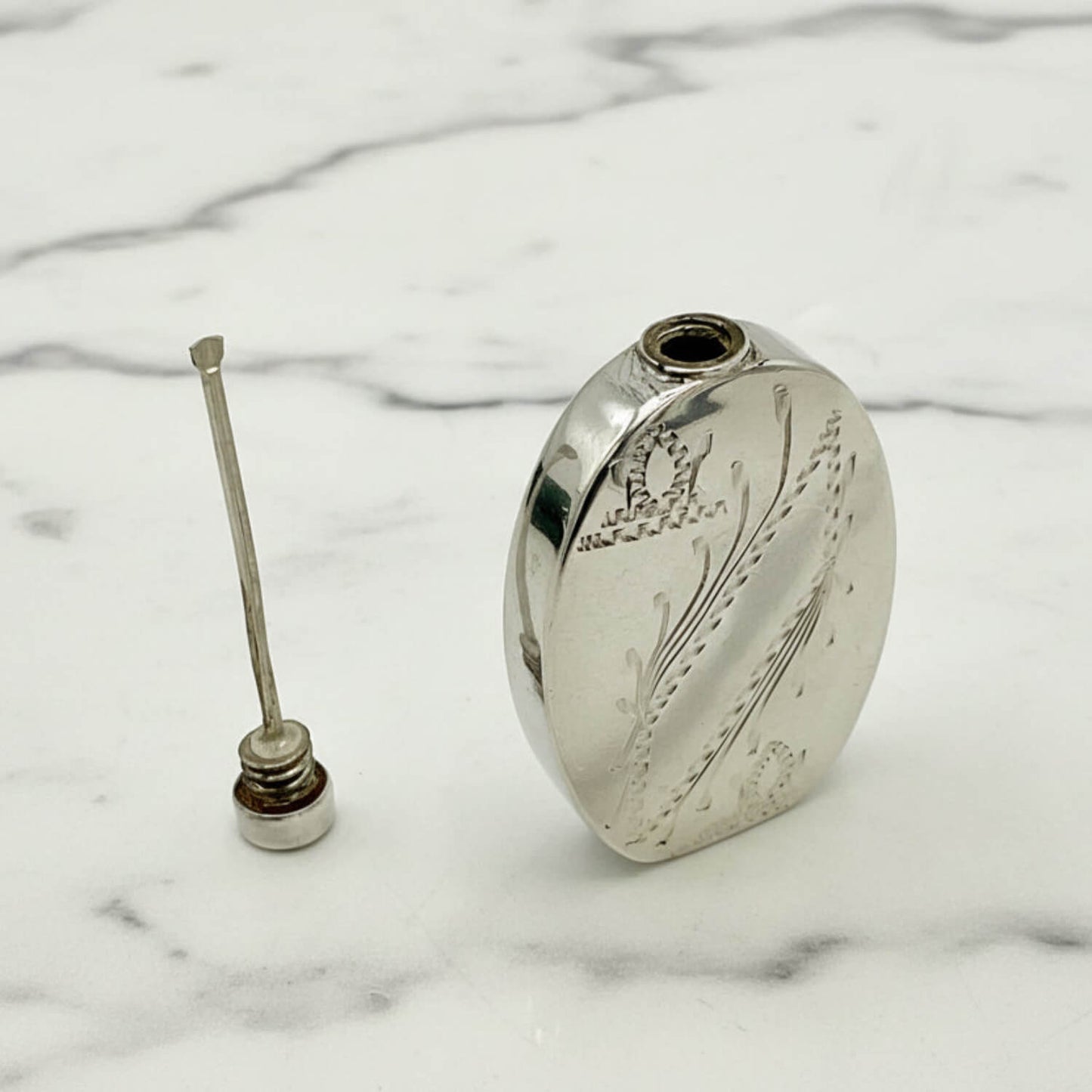 Small Sterling Silver Scent Bottle with engraved  design on a marble surface