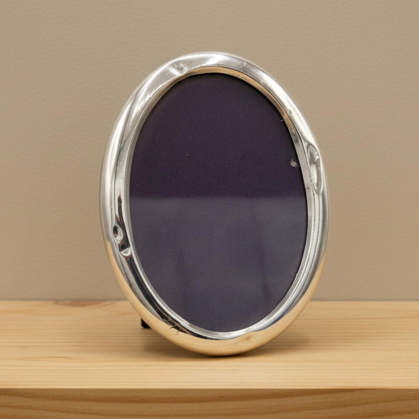 oval photo frame on a wooden surface with a beige background