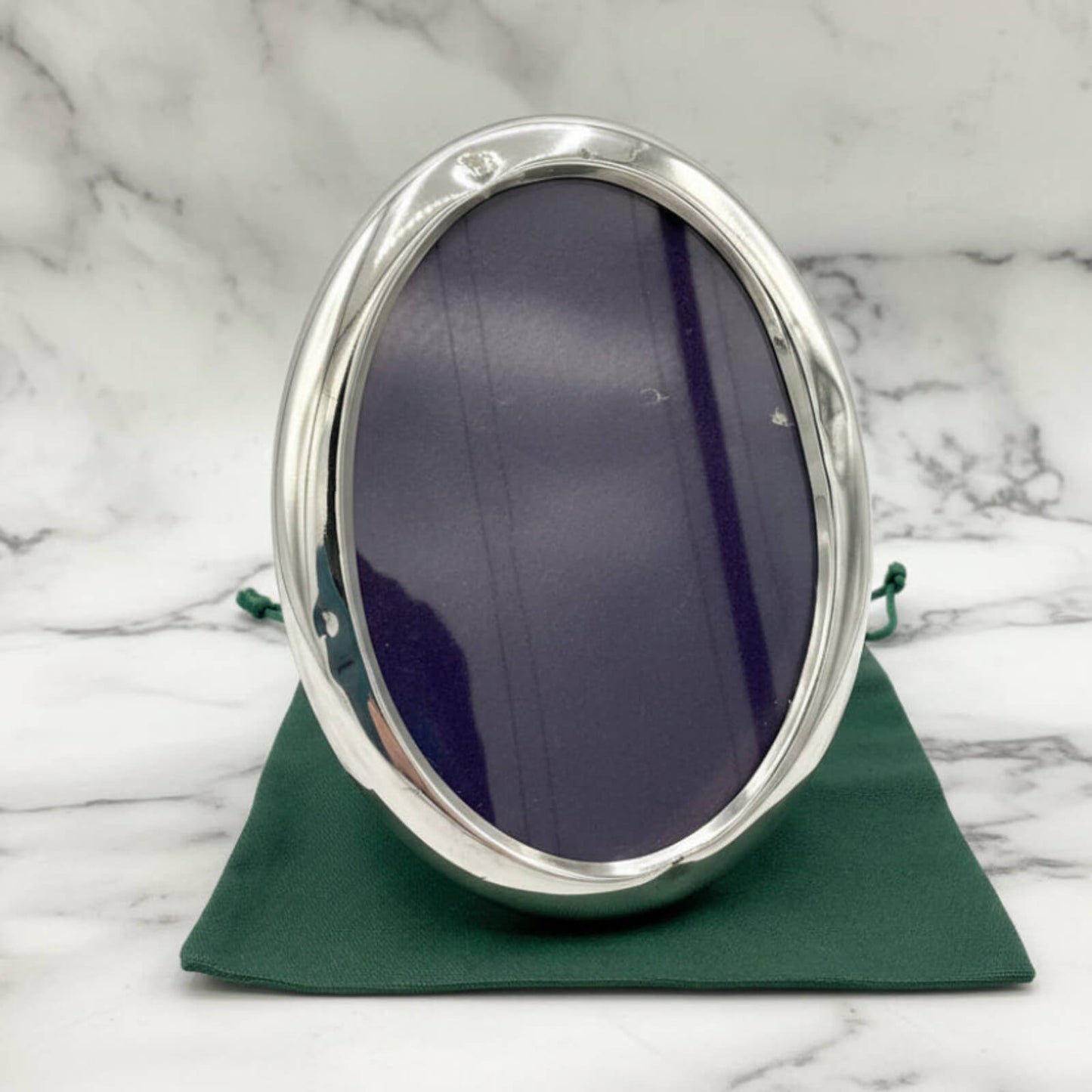 Silver oval photo frame on a green bag with a marble background
