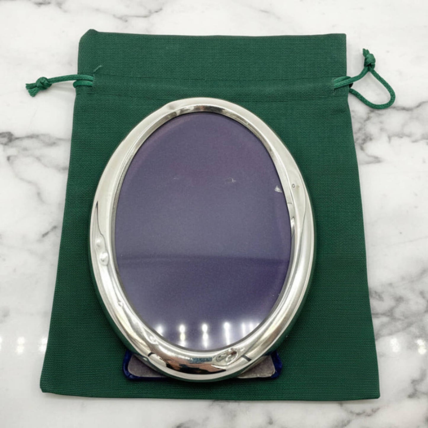 Silver oval photo frame on a green fabric pouch with a marble background