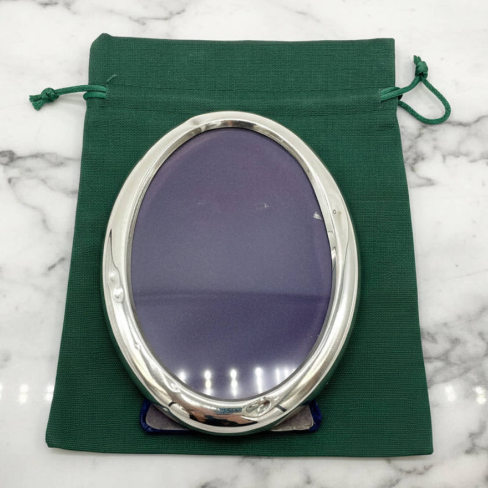 Silver oval photo frame on a green fabric pouch with a marble background
