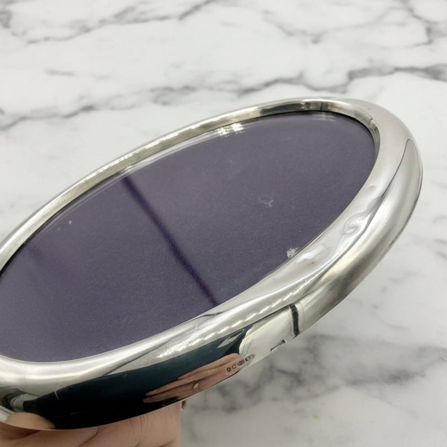 side of oval photo frame with purple reflective surface on a marble background