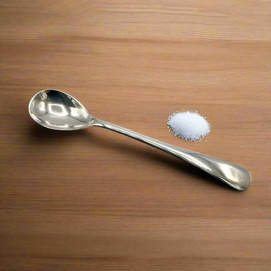 Silver spoon next to a small pile of salt on a wooden surface