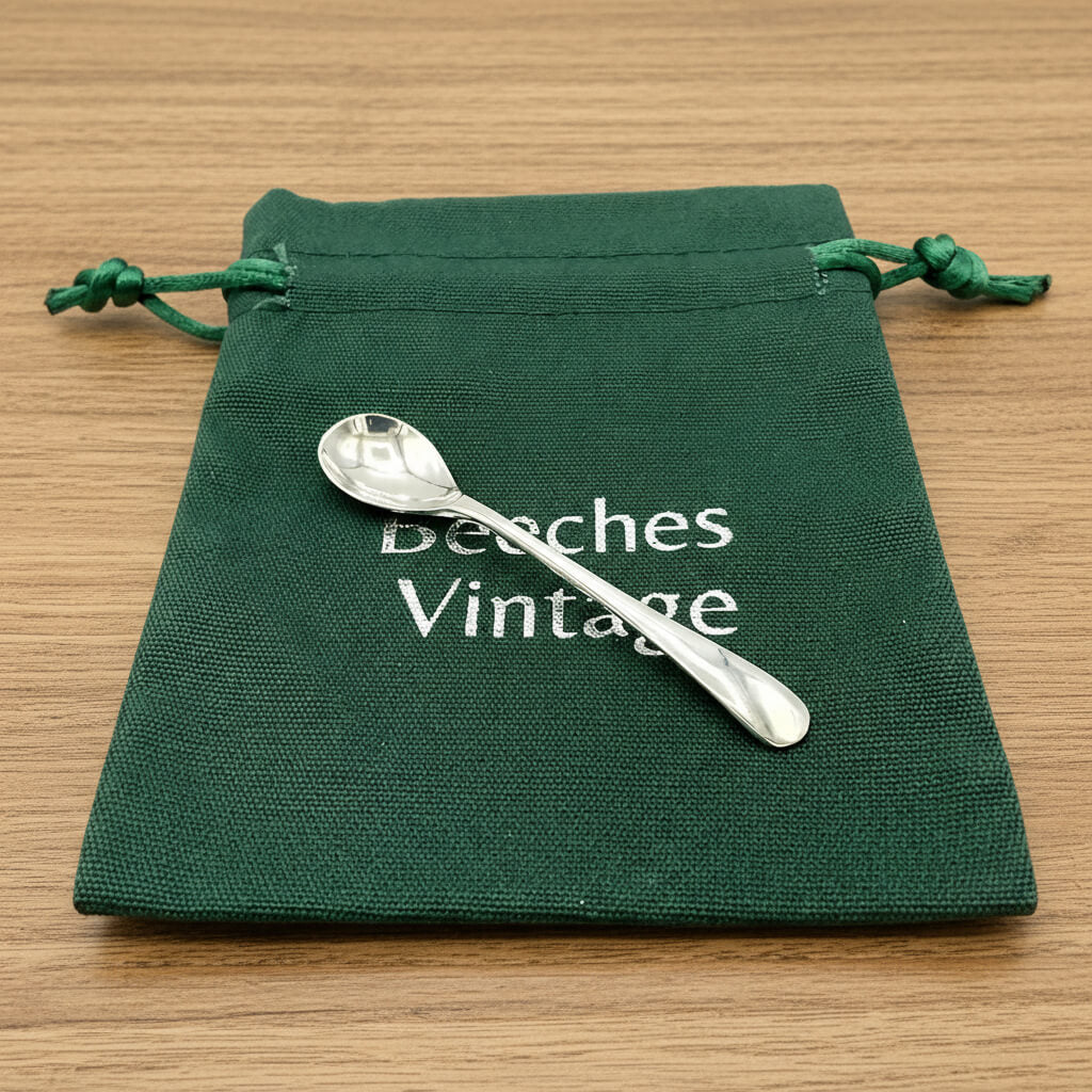 Silver spoon on a green drawstring bag with 'Beeches Vintage' text on a wooden surface