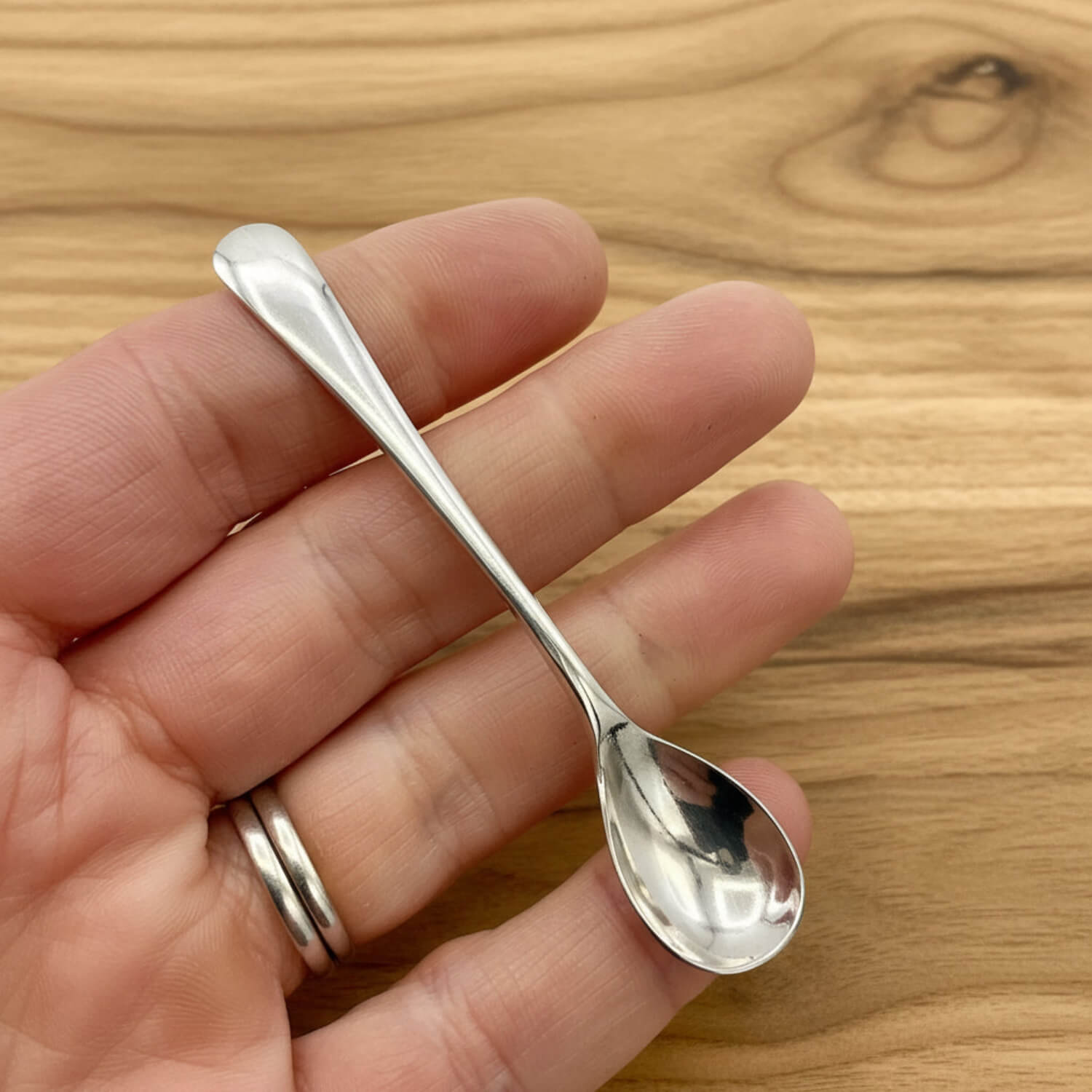 Small silver spoon held between fingers on a wooden surface