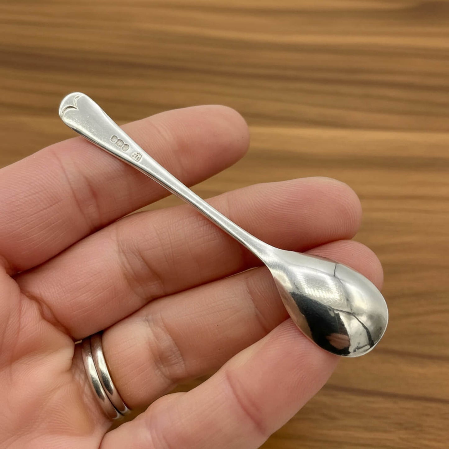 Silver spoon held in a hand with a wooden background