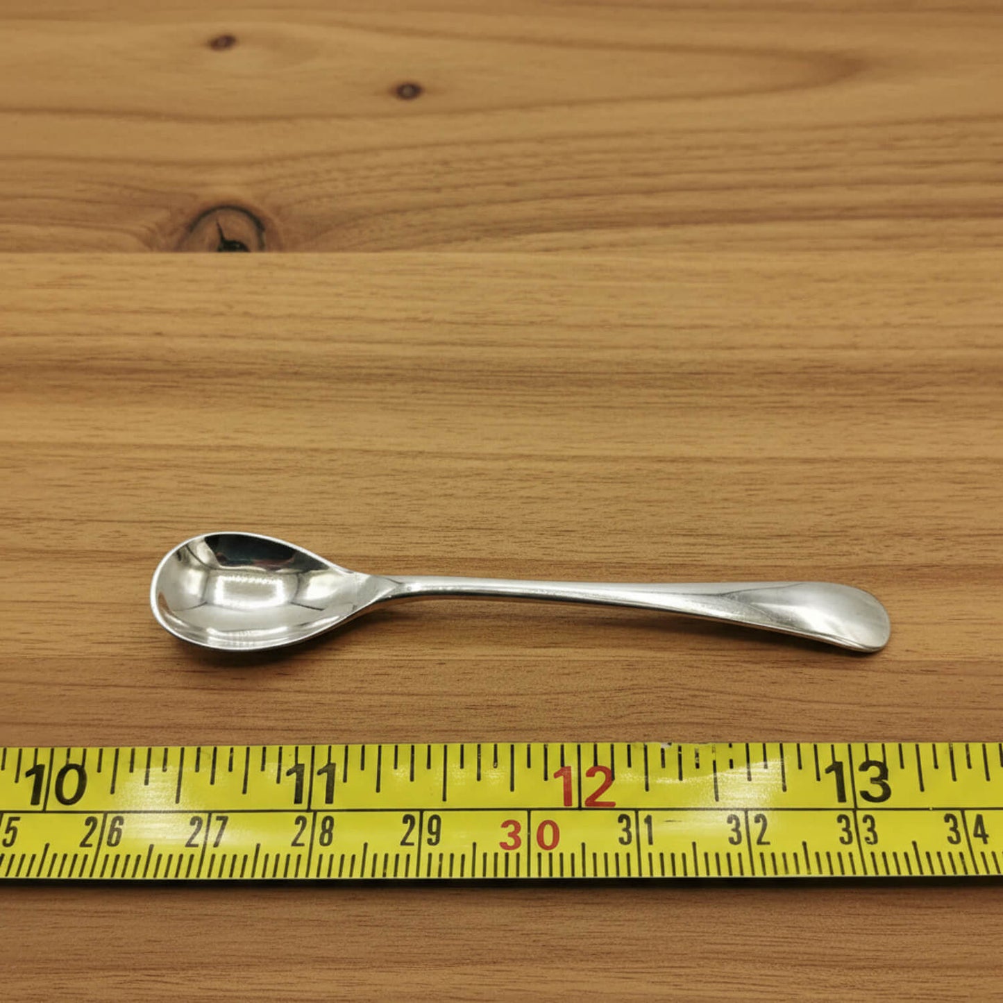Silver spoon on a wooden surface with a yellow measuring tape for scale.