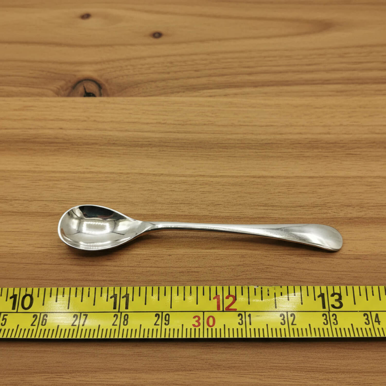Silver spoon on a wooden surface with a yellow measuring tape for scale.