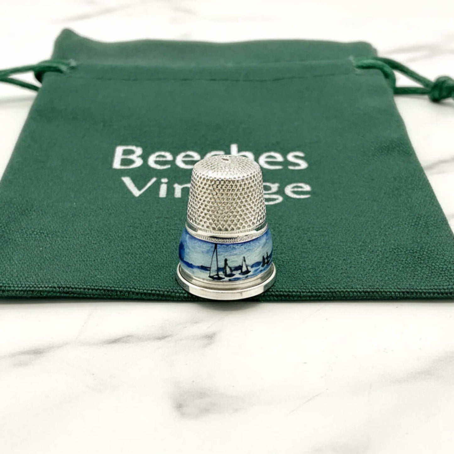 Silver thimble with blue boat and windmill design on a green drawstring bag with 'Beeches Vintage' text.