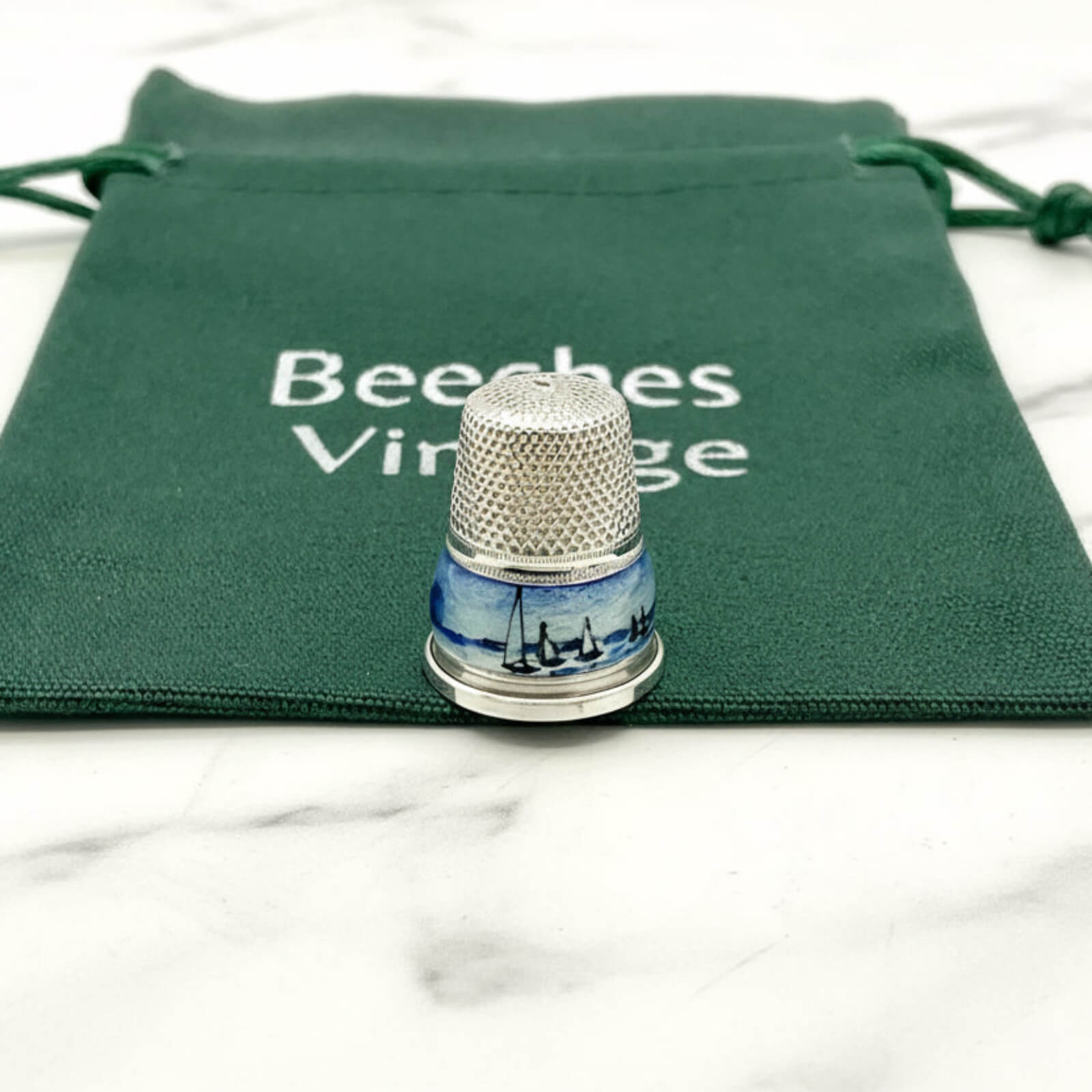 Silver thimble with blue boat and windmill design on a green drawstring bag with 'Beeches Vintage' text.