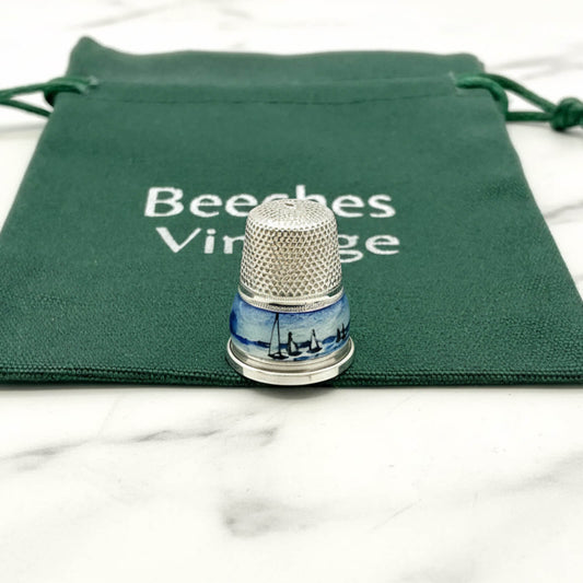Silver thimble with blue boat and windmill design on a green drawstring bag with 'Beeches Vintage' text.