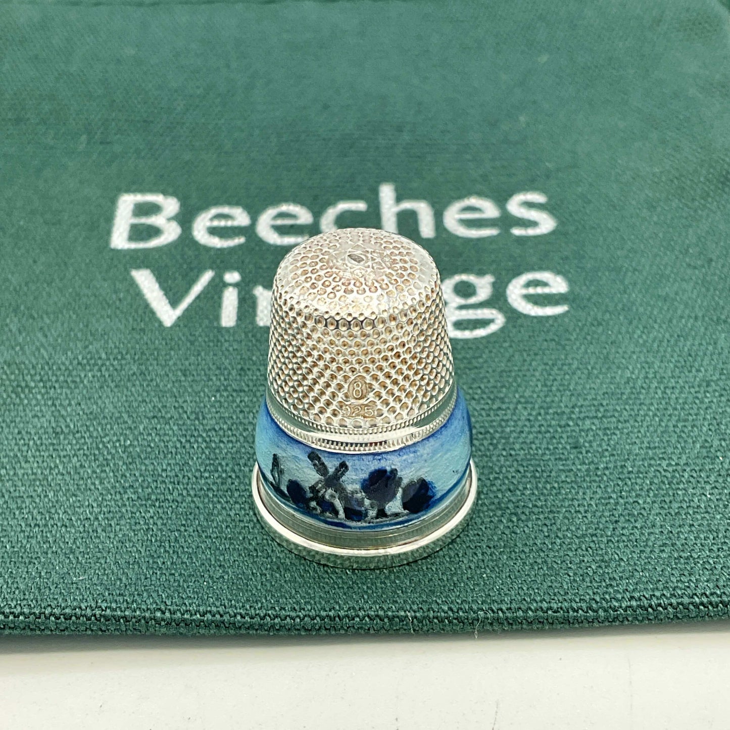 Decorative thimble with blue windmill design on a green fabric bag background with 'Beeches Vintage' branding.