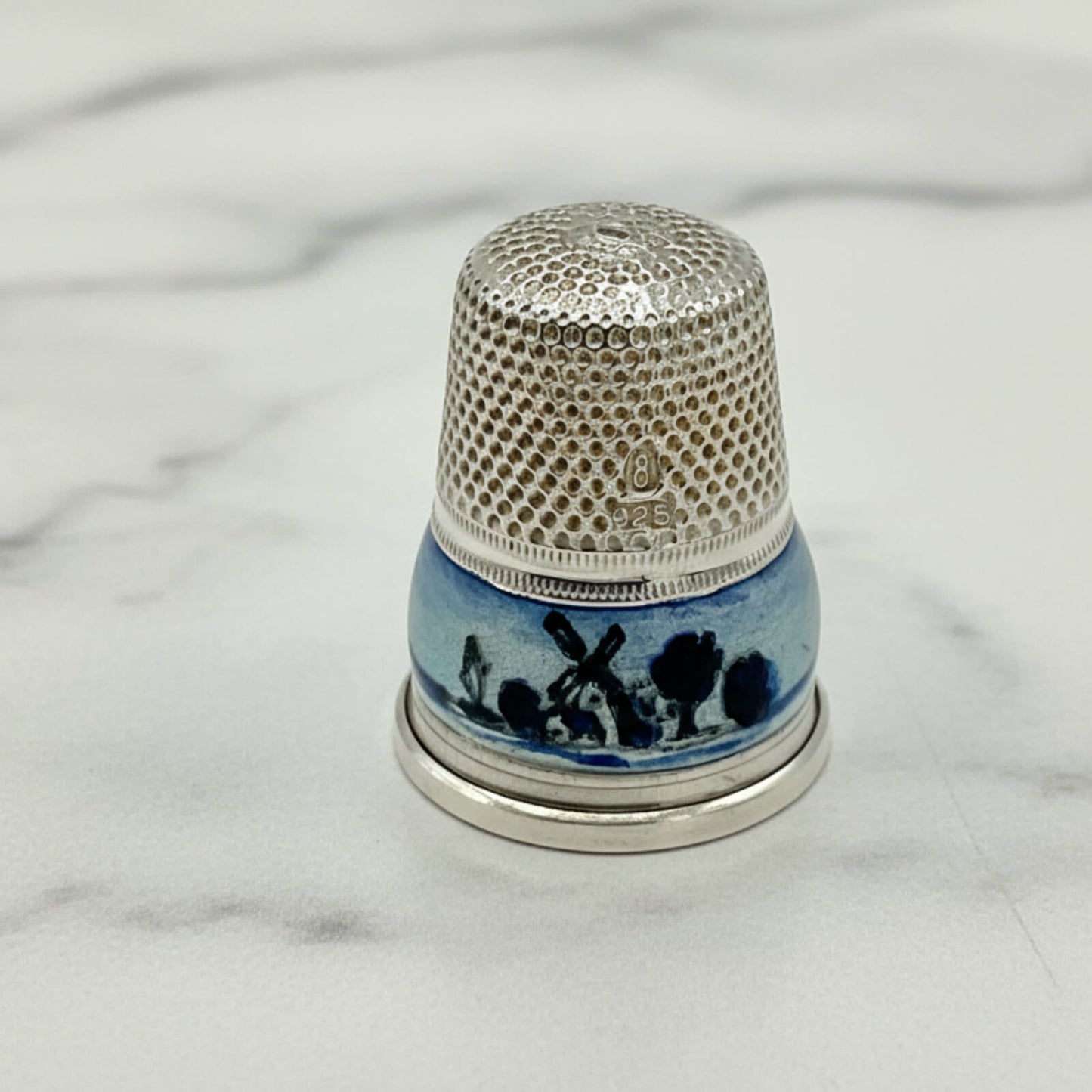 Silver Thimble with decorative blue and white design on a marble surface
