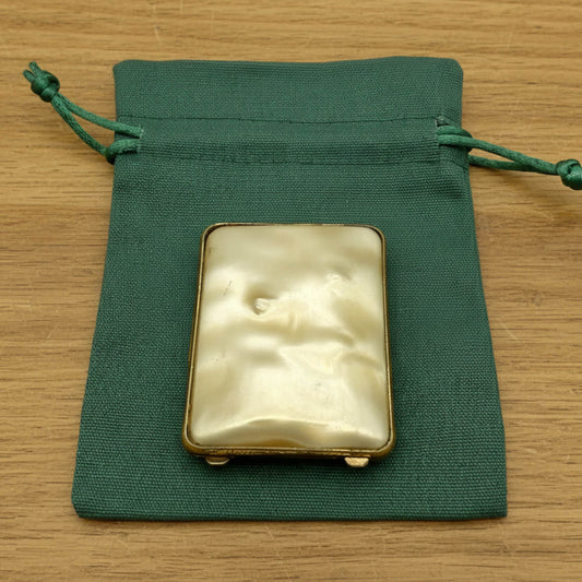 Rectangular case with brass frame on a green drawstring bag on a wooden surface