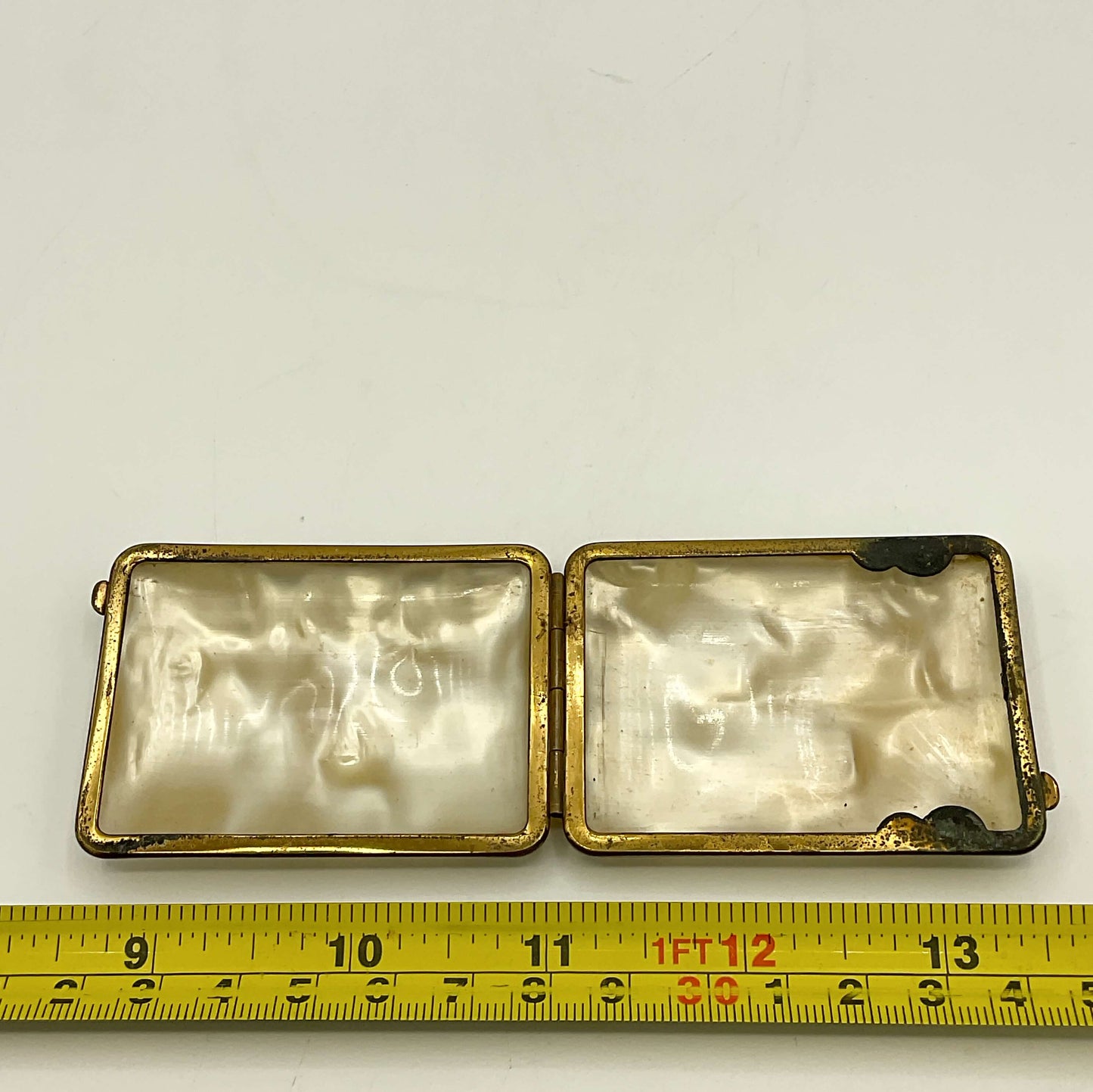 rectangular case with a brass frame on a white background, accompanied by a yellow measuring tape for scale.