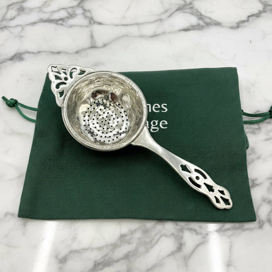 Silver tea strainer on a green cloth with a marble background