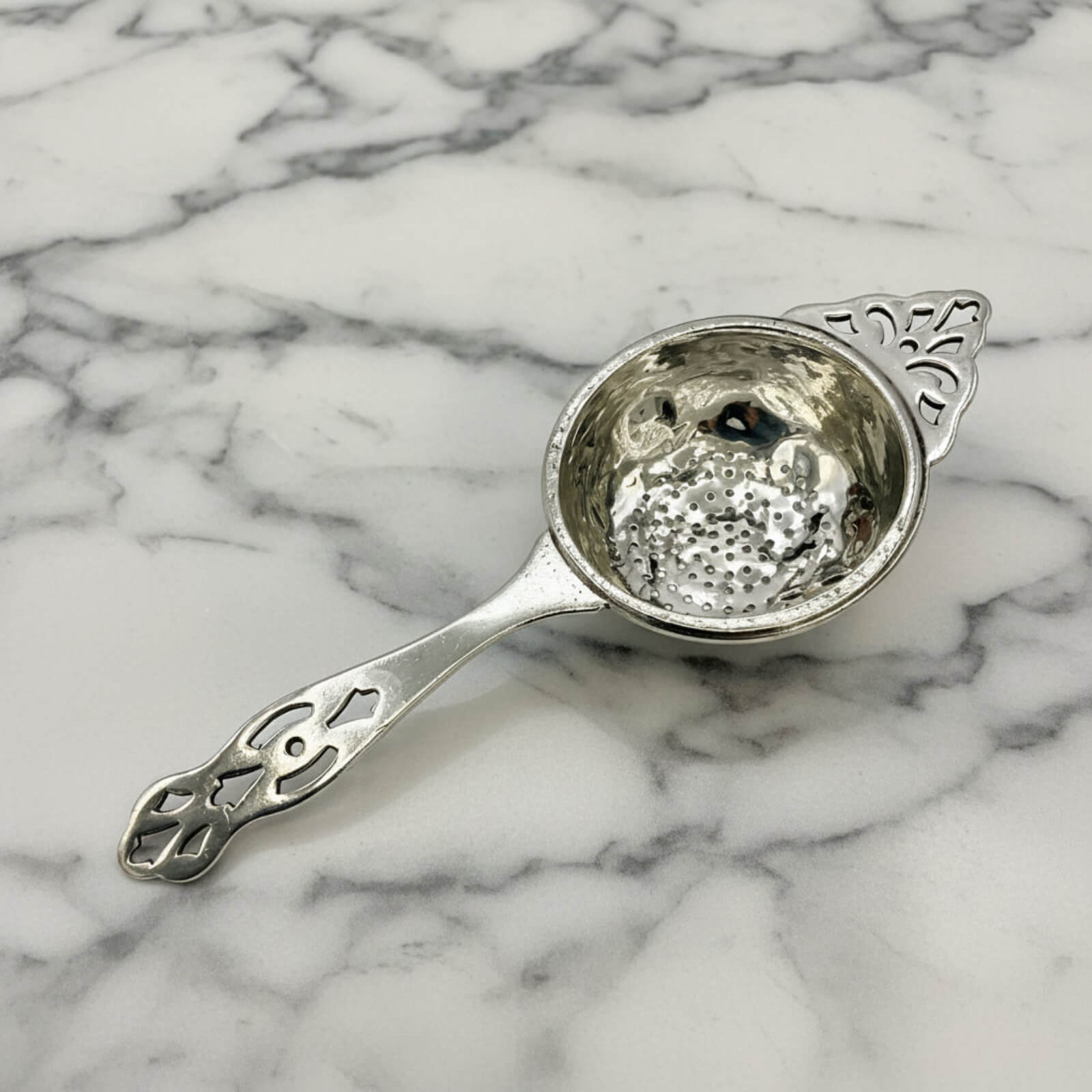 Decorative silver tea strainer on a marble surface