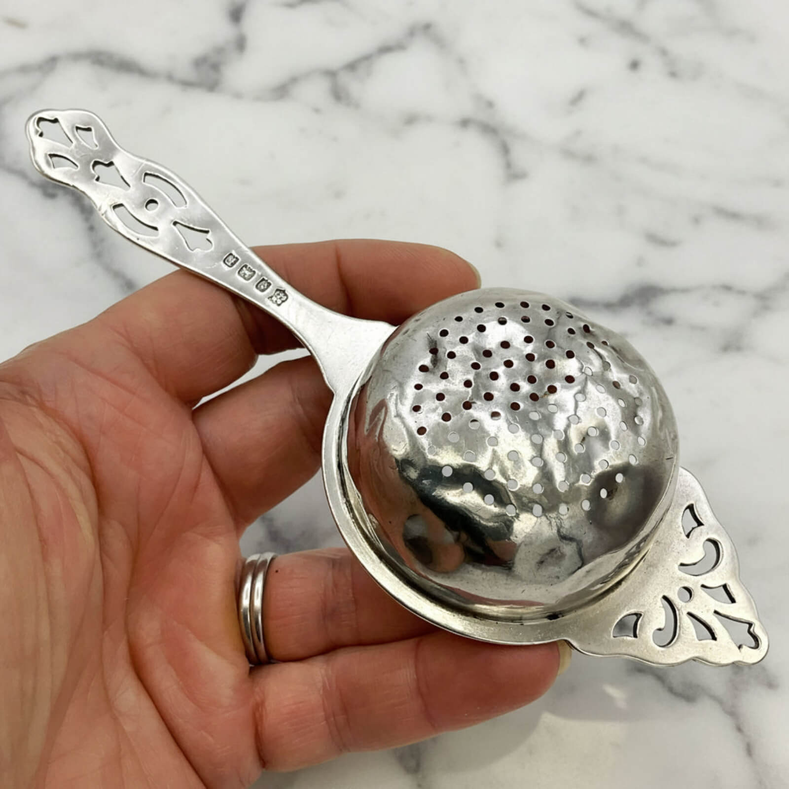 Silver tea strainer held in a hand against a marble background