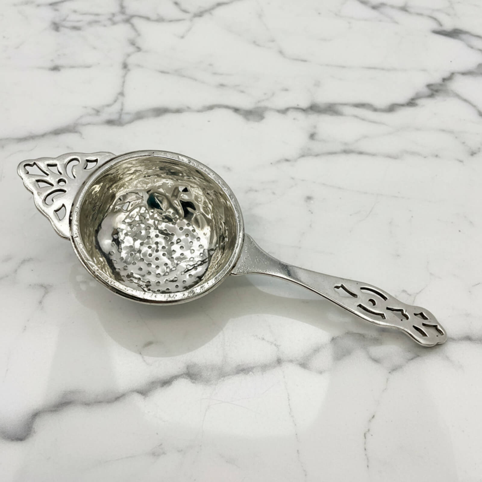 Silver tea strainer on a marble surface