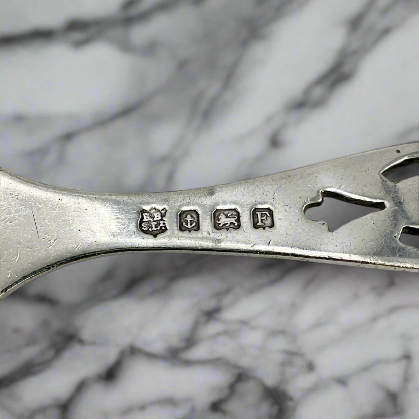 Close-up of a silver spoon with engraved marks on a marble surface