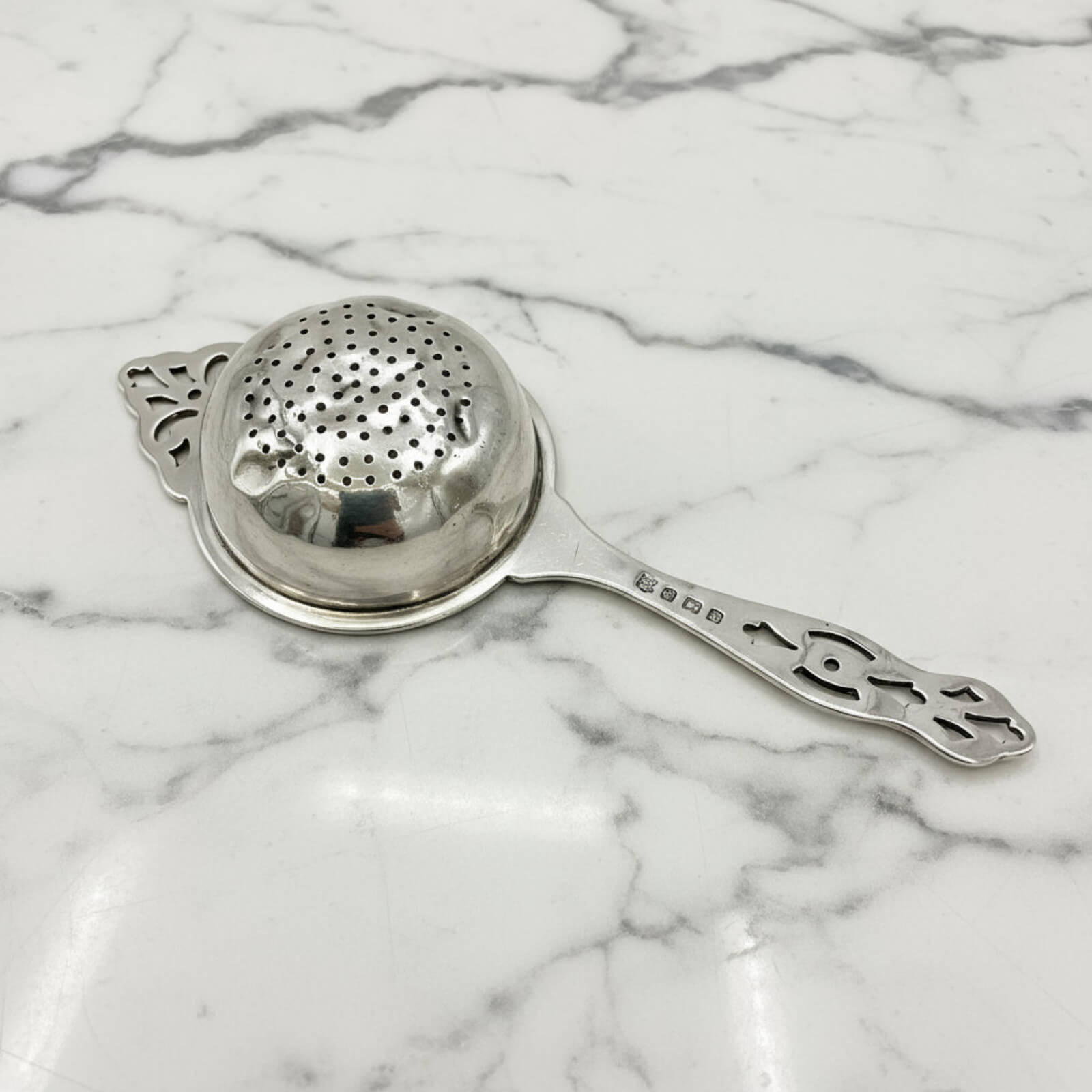 Silver tea strainer on a marble surface