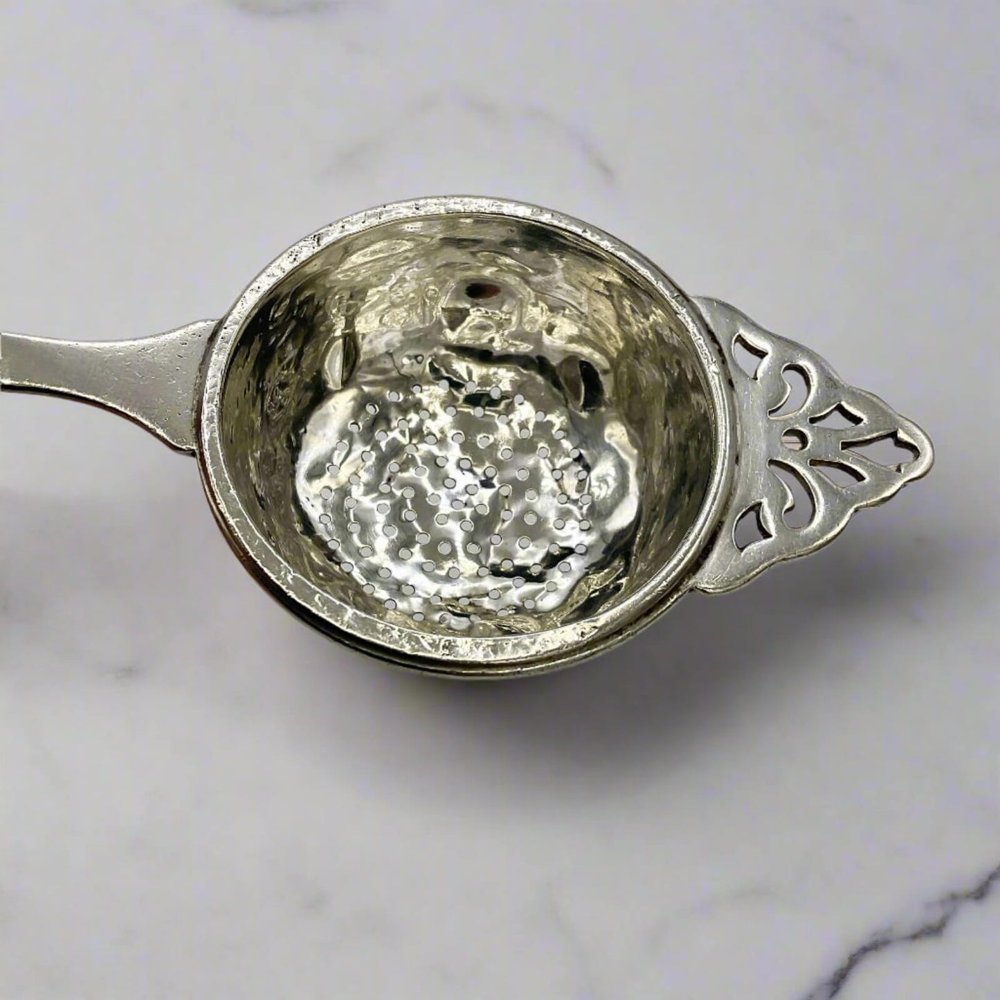 Silver tea strainer on a marble surface