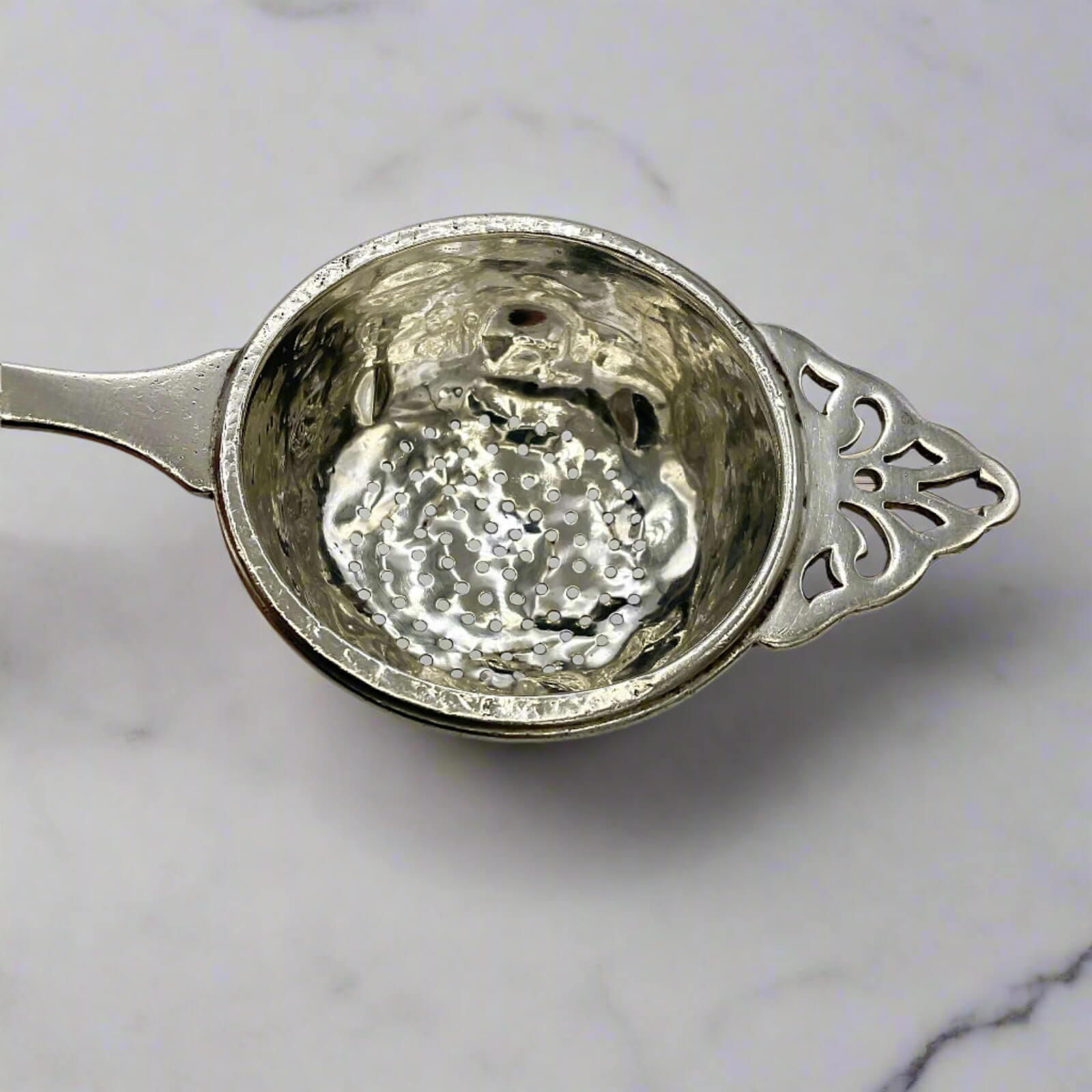 Silver tea strainer on a marble surface