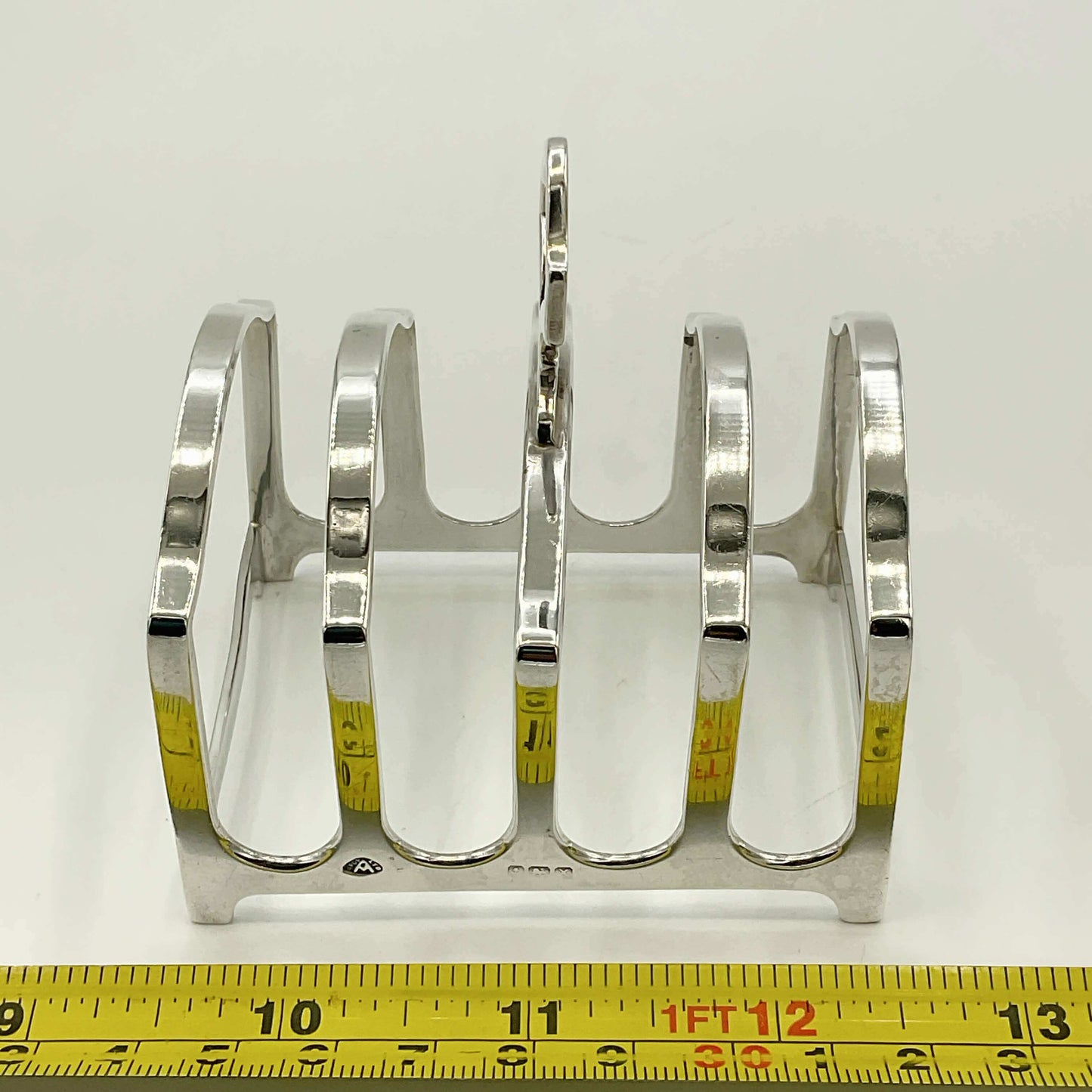 Silver toast rack with a measuring tape for scale on a white background