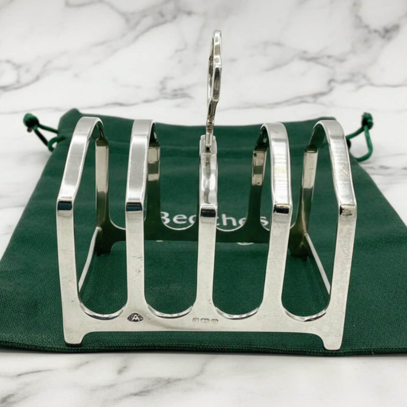 Silver toast rack on a green cloth bag with a marble background