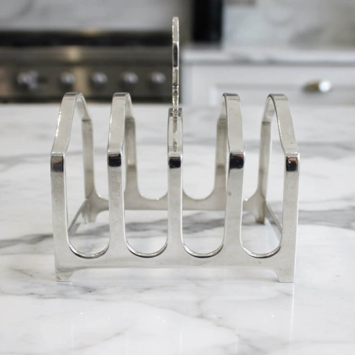 Silver toast rack on a marble surface with a blurred kitchen background