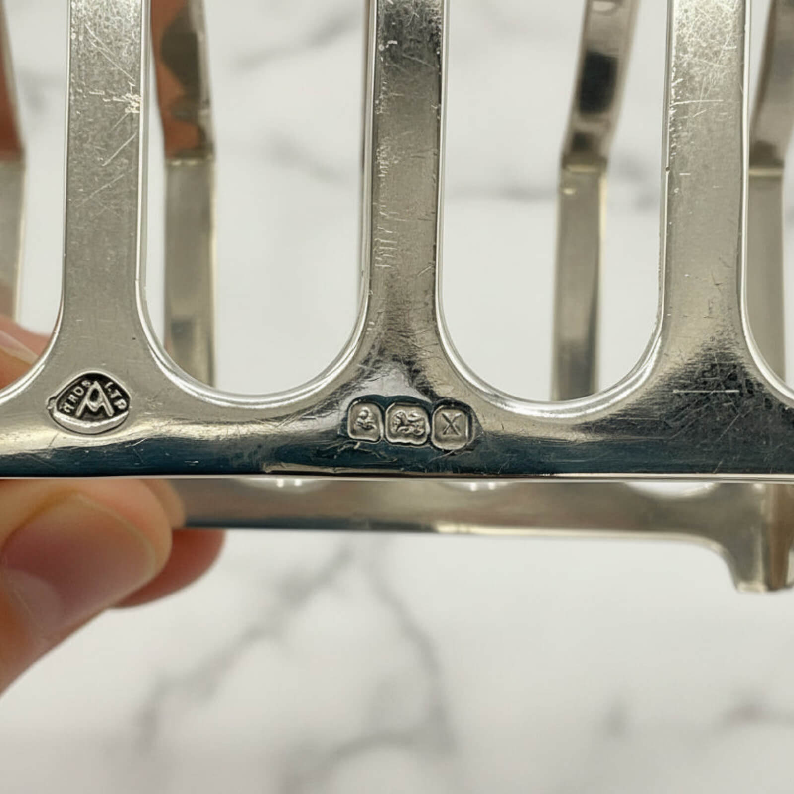 Close-up of a silver toast rack with visible hallmarks on a white background