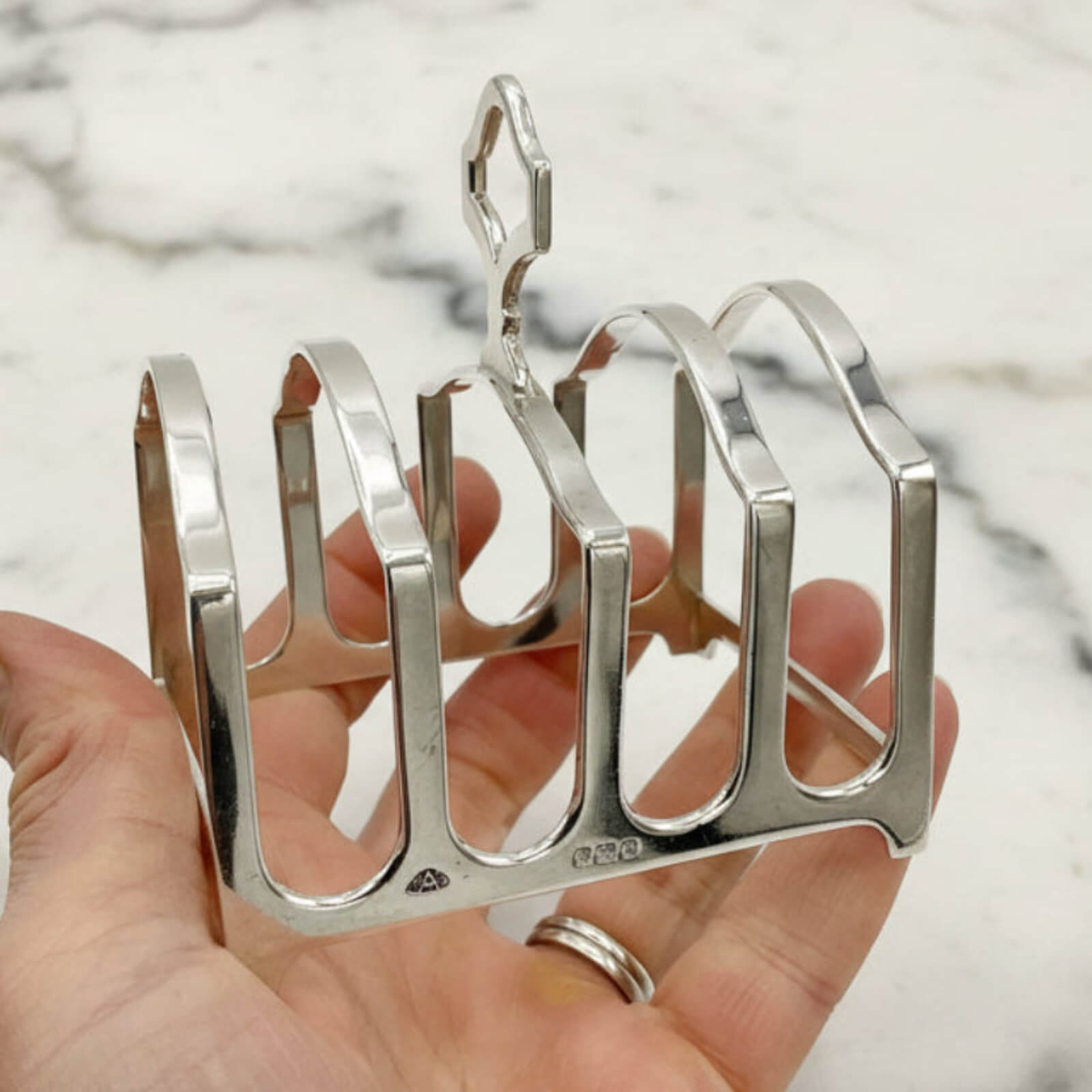 Silver toast rack held in a hand with a marble background