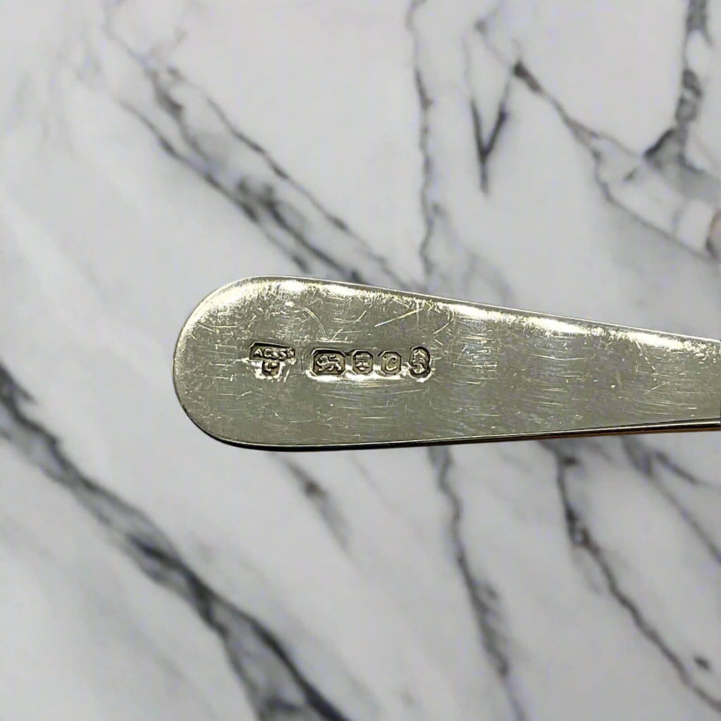 Silver spoon handle with hallmark details on a marble background