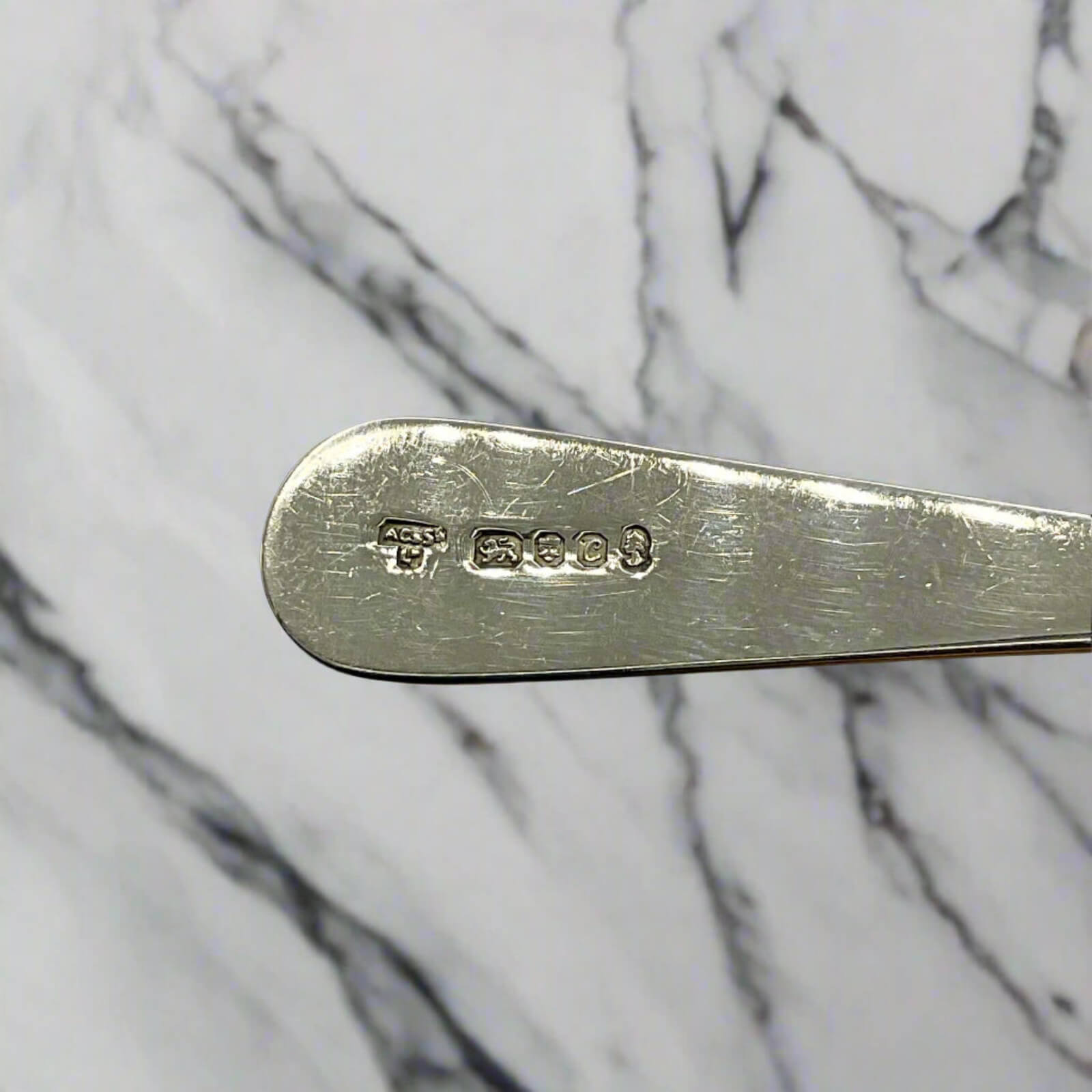 Silver spoon handle with hallmark details on a marble background