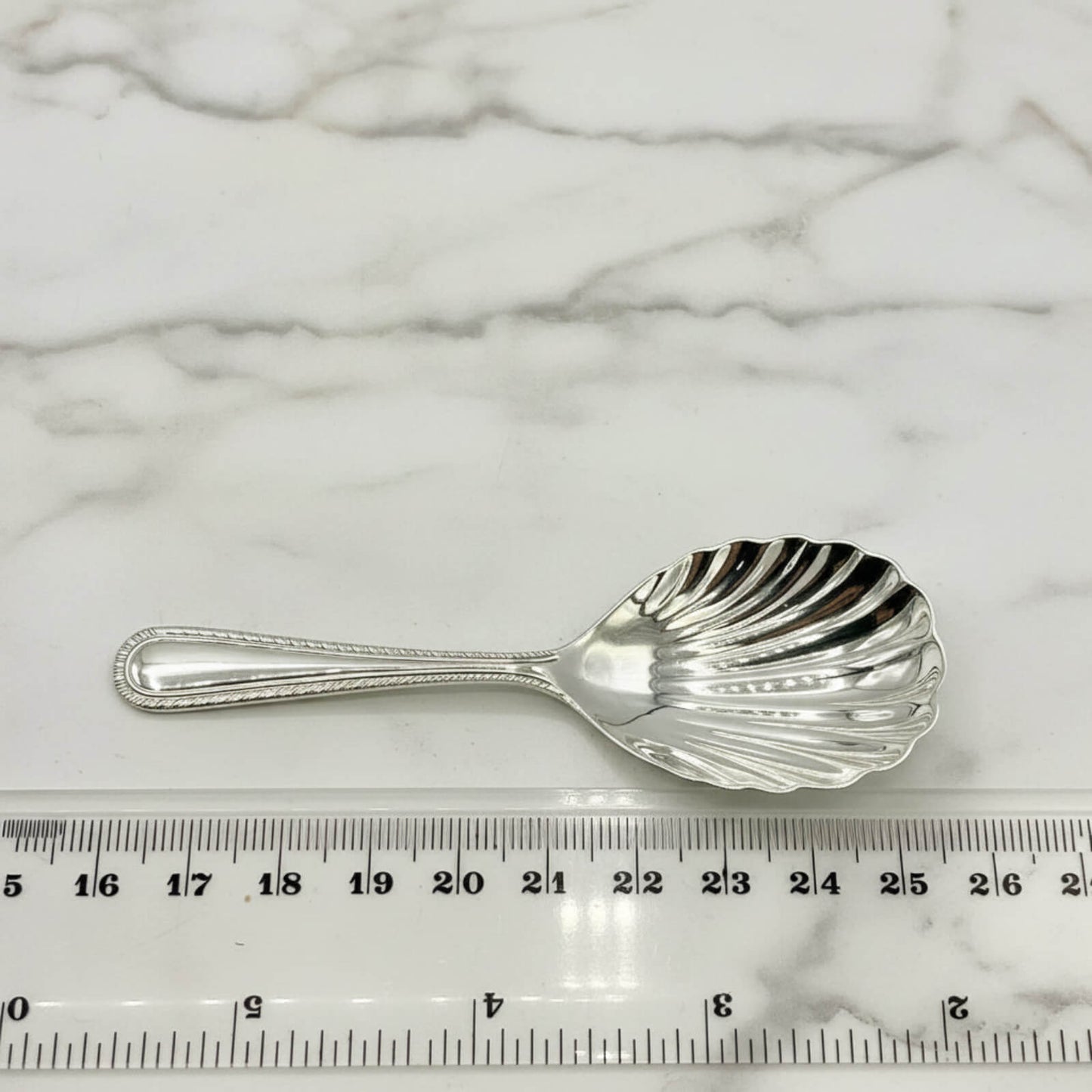 Vintage 1977 Sterling Silver Tea Caddy Spoon next to a tape measure on a marble background